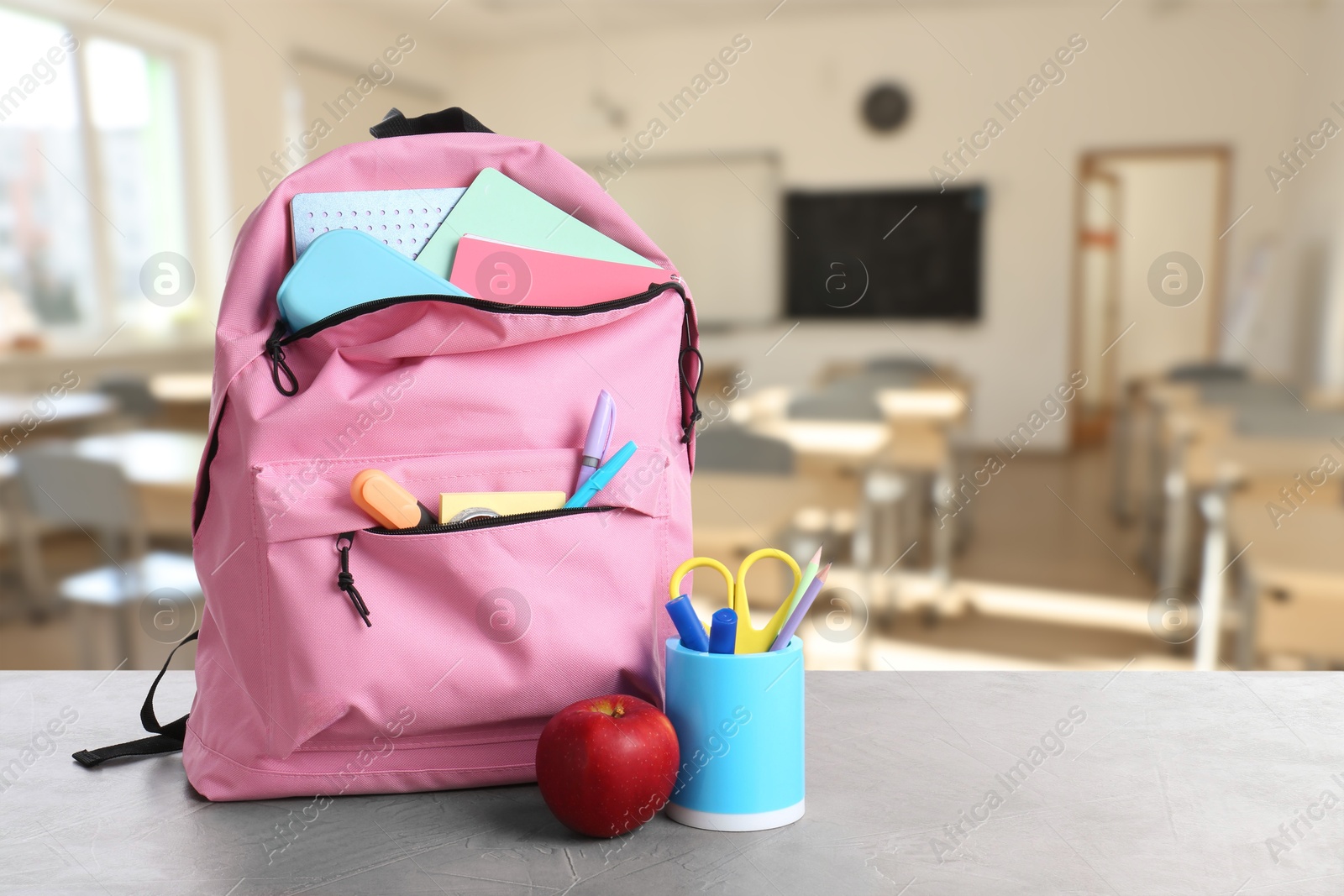 Image of Pink backpack with stationery on school desk in classroom. Space for text