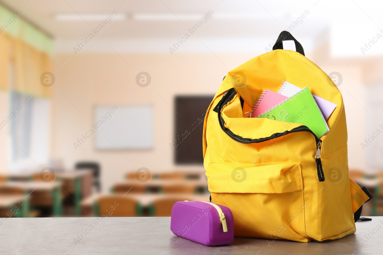 Image of Yellow backpack with stationery on school desk in classroom. Space for text