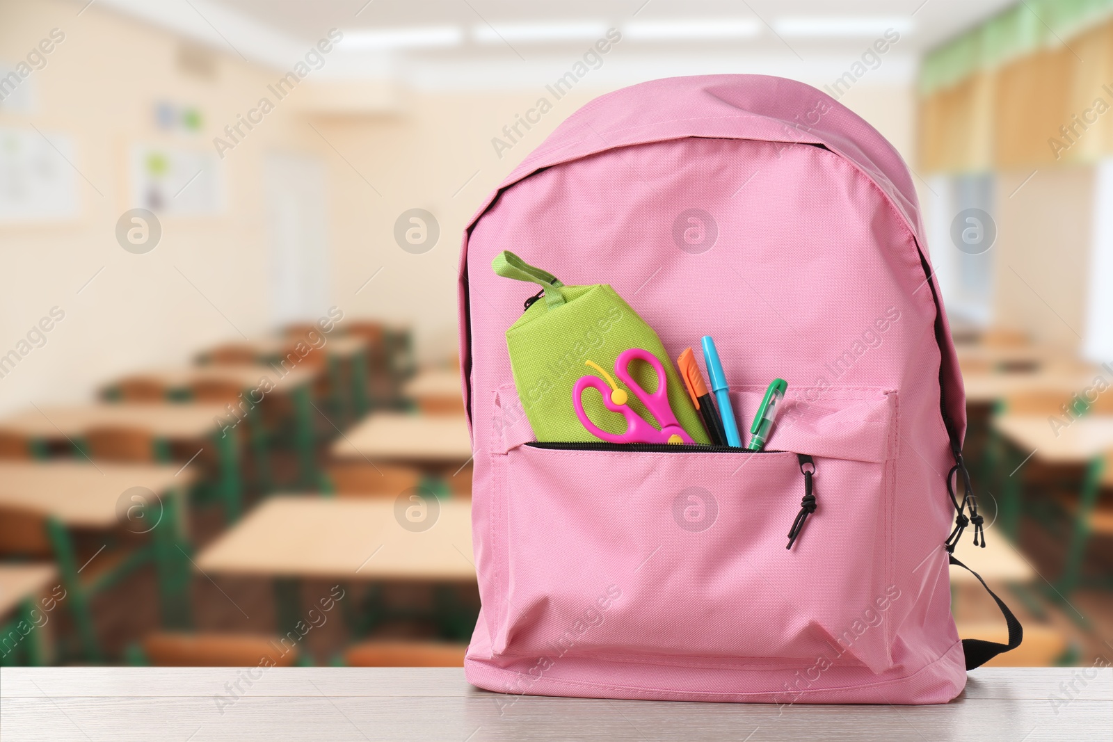 Image of Pink backpack with stationery on school desk in classroom. Space for text