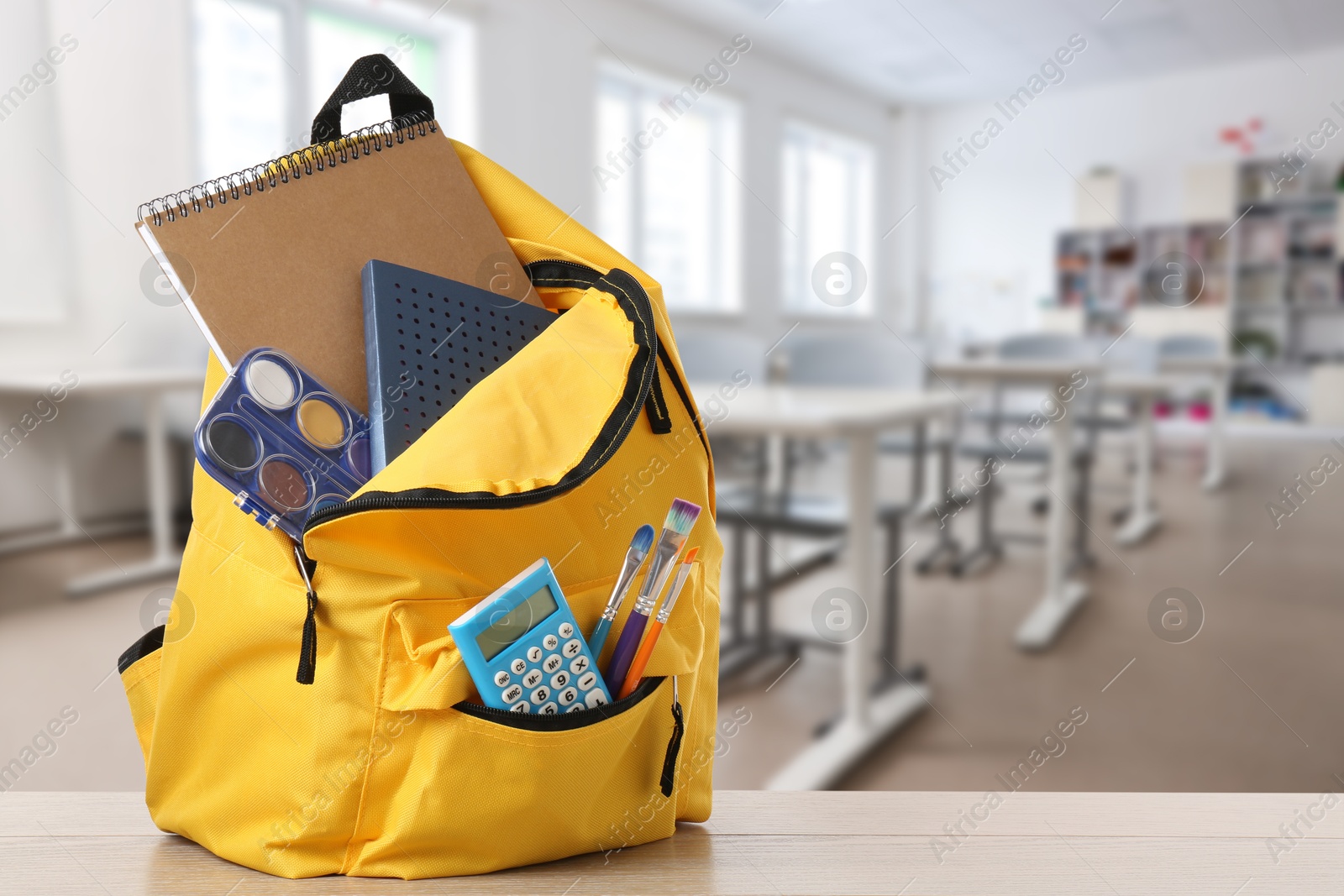 Image of Yellow backpack with stationery on school desk in classroom. Space for text