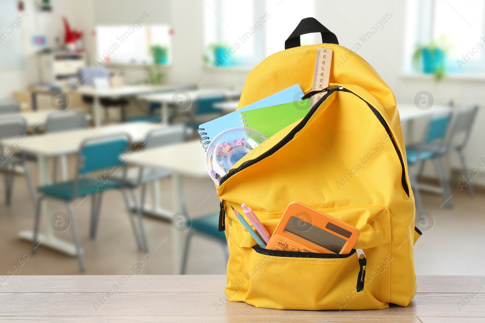 Image of Yellow backpack with stationery on school desk in classroom. Space for text