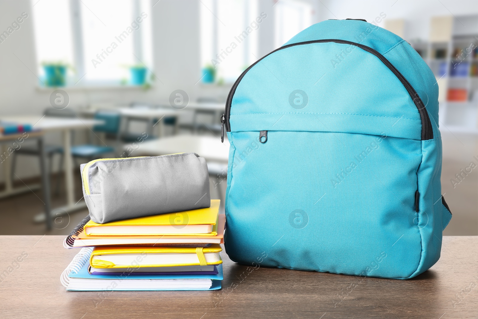 Image of Light blue backpack with stationery on school desk in classroom. Space for text