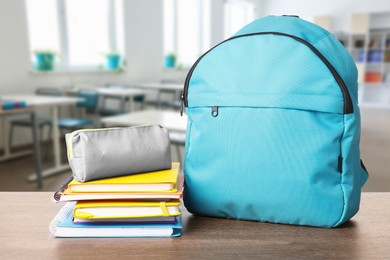 Image of Light blue backpack with stationery on school desk in classroom. Space for text