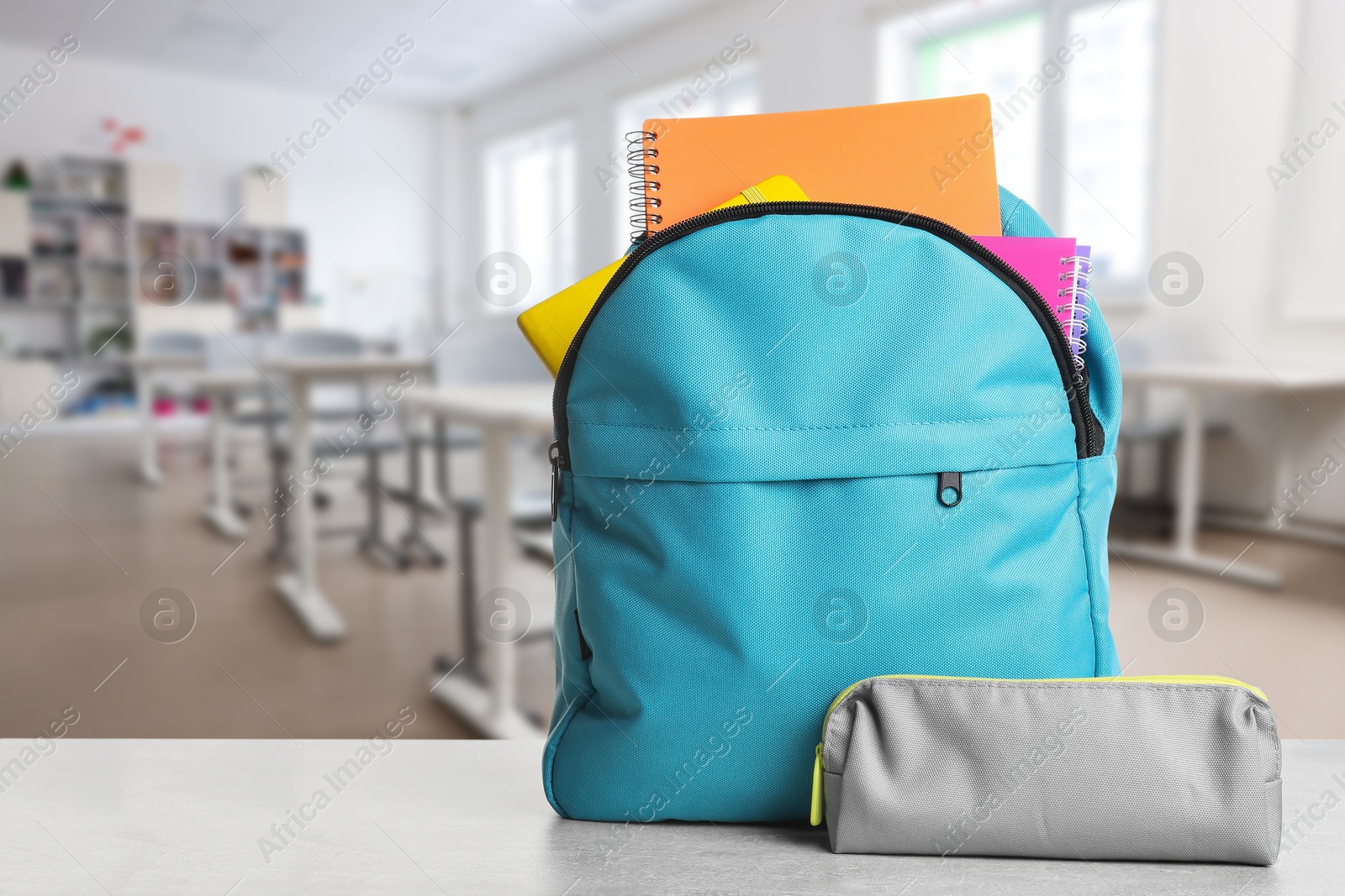 Image of Light blue backpack with stationery on school desk in classroom. Space for text