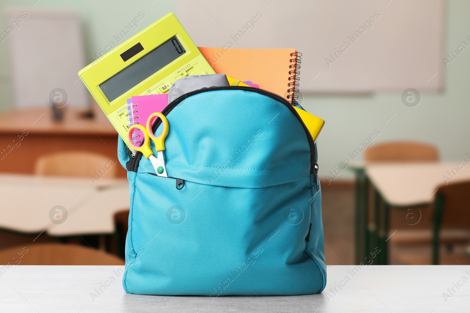 Image of Light blue backpack with stationery on school desk in classroom