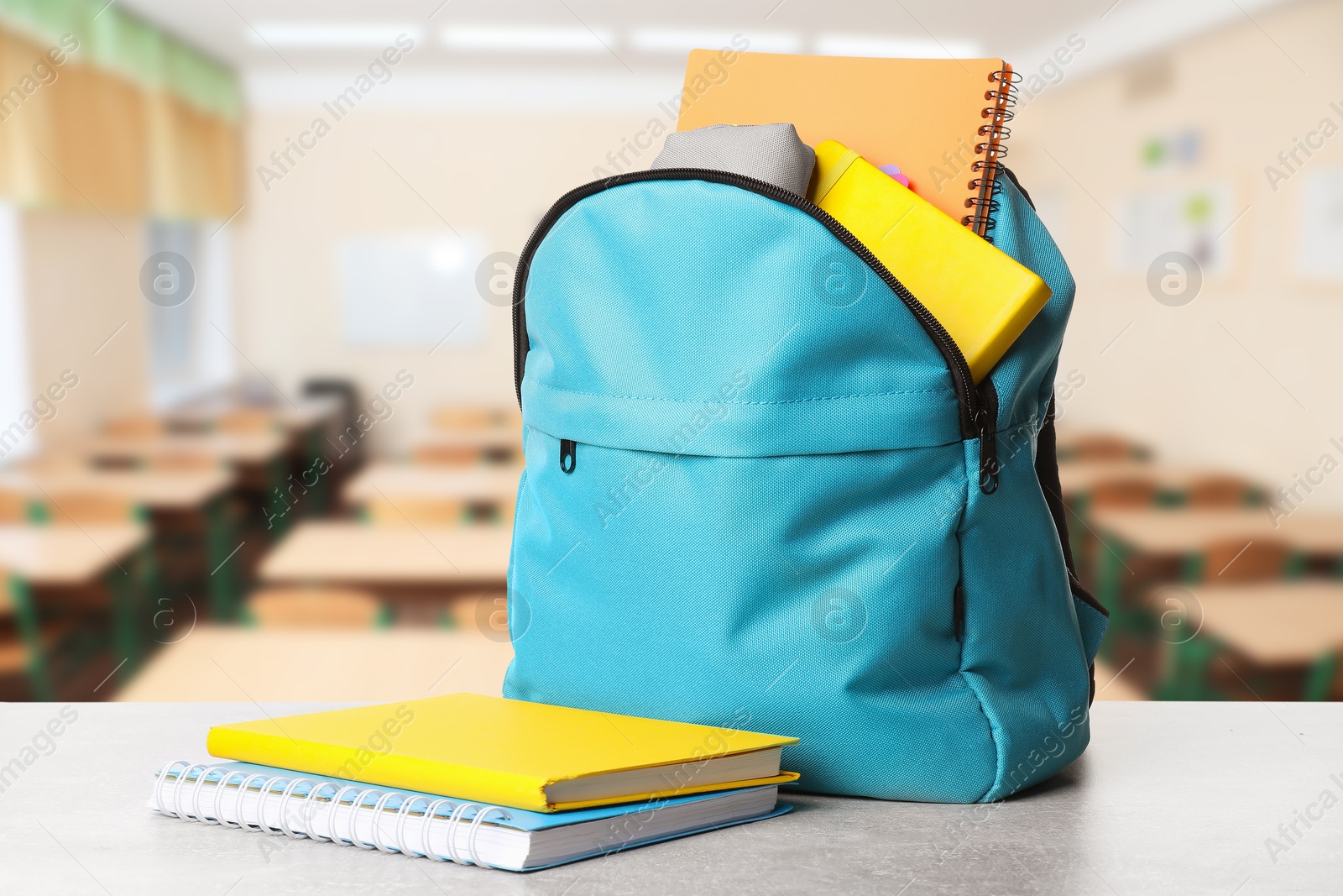 Image of Light blue backpack with stationery on school desk in classroom