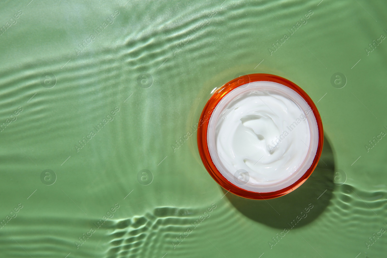 Photo of Cosmetic product. Jar with cream in water on light green background, top view. Space for text