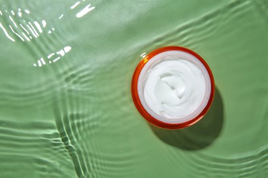 Photo of Cosmetic product. Jar with cream in water on light green background, top view. Space for text