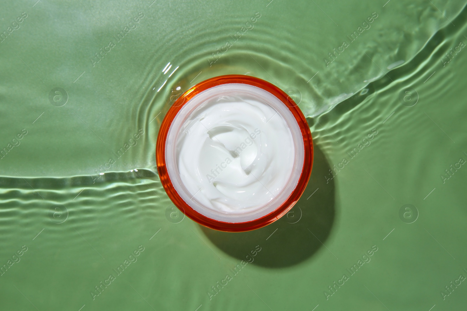 Photo of Jar with cream in water on light green background, top view. Cosmetic product