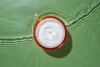 Jar with cream in water on light green background, top view. Cosmetic product