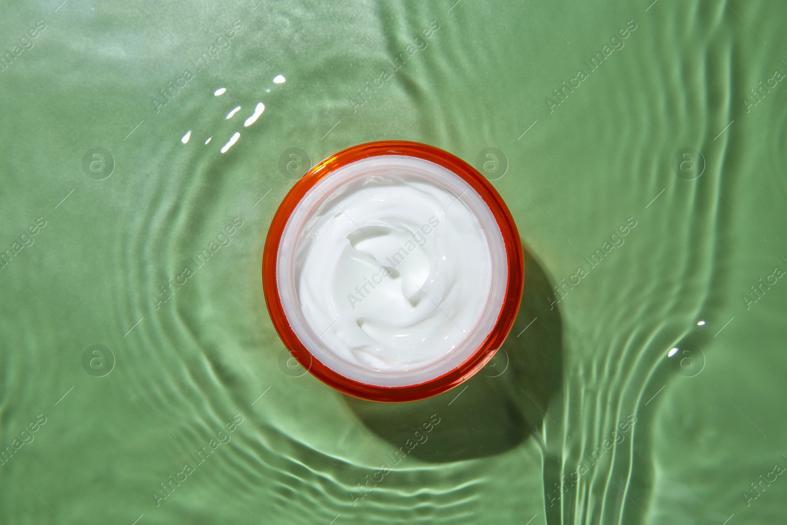 Photo of Jar with cream in water on light green background, top view. Cosmetic product