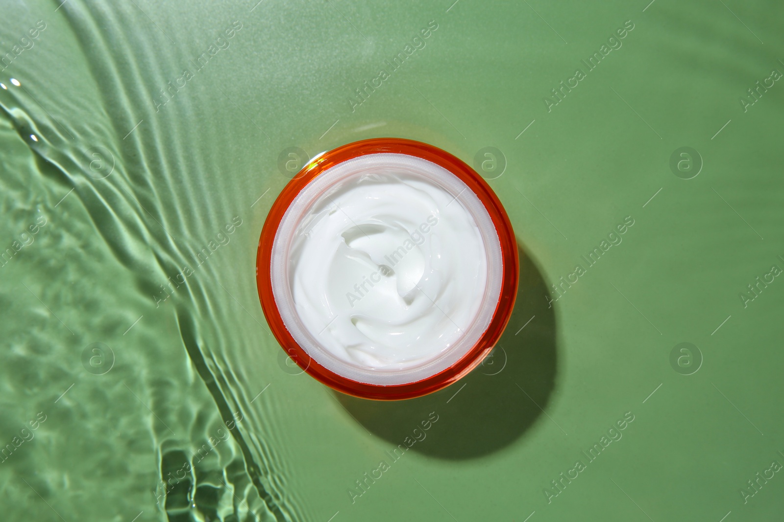 Photo of Jar with cream in water on light green background, top view. Cosmetic product