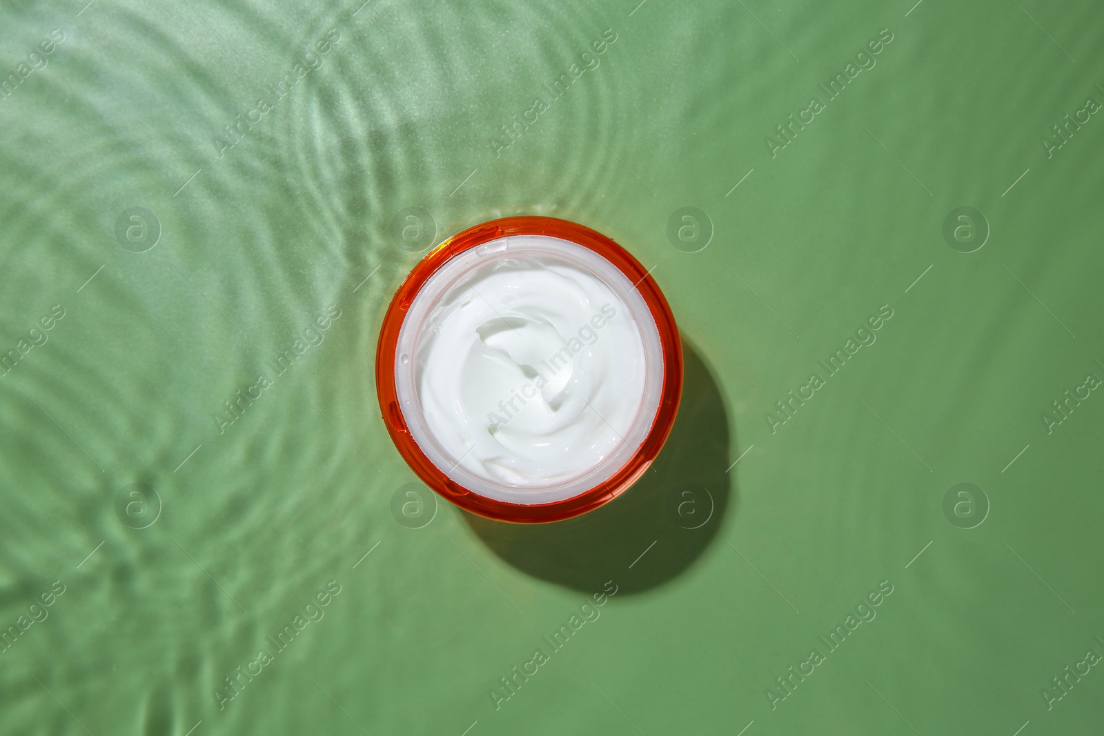 Photo of Jar with cream in water on light green background, top view. Cosmetic product