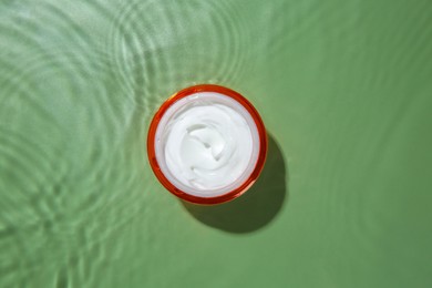 Jar with cream in water on light green background, top view. Cosmetic product