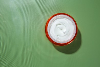 Cosmetic product. Jar with cream in water on light green background, top view. Space for text