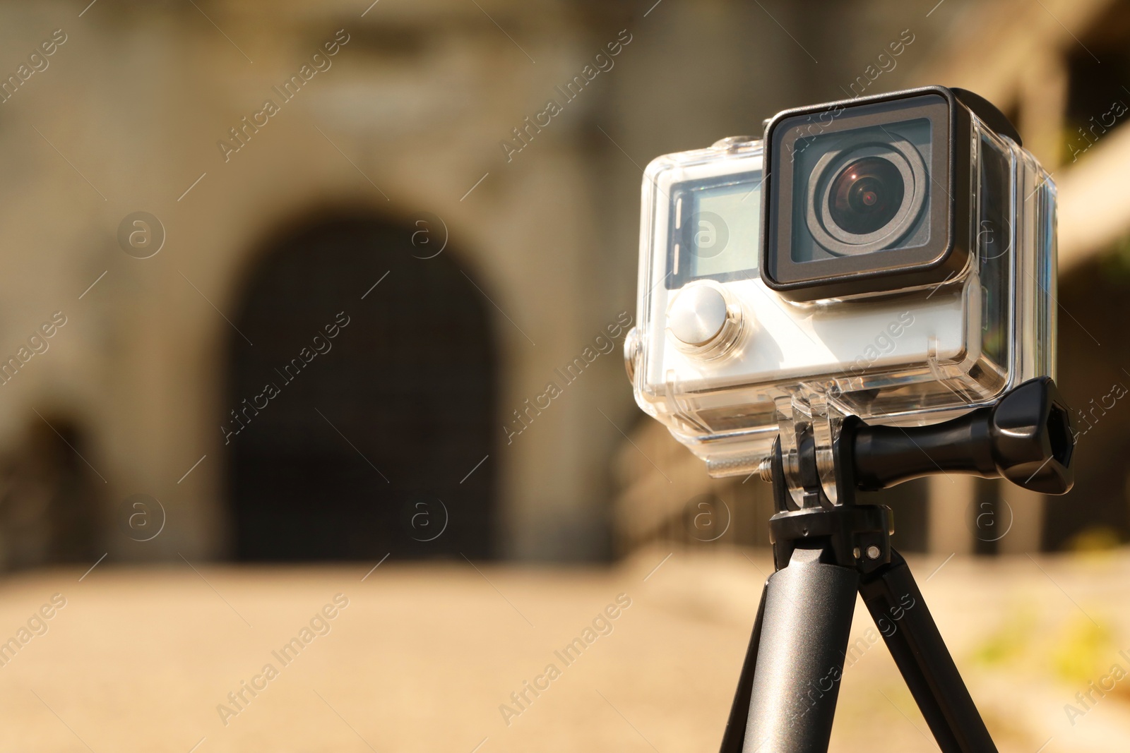 Photo of Modern action camera with tripod on blurred background, closeup. Space for text