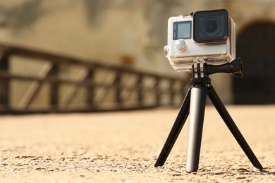 Photo of Modern action camera with tripod outdoors. Space for text