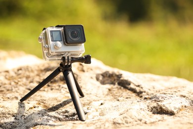 Modern action camera with tripod on stone outdoors, space for text