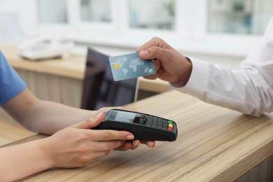 Receptionist taking payment from client via terminal at hospital, closeup