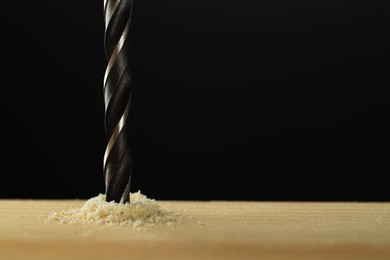 Photo of Drilling hole in wooden plank on black background, closeup. Space for text