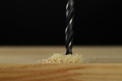 Drilling hole in wooden plank on black background, closeup