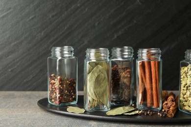 Different spices in glass jars on grey wooden table, closeup