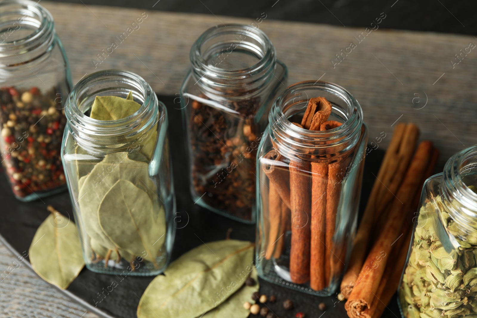 Photo of Different spices in glass jars on grey wooden table, closeup