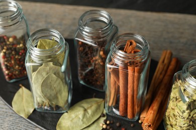 Different spices in glass jars on grey wooden table, closeup