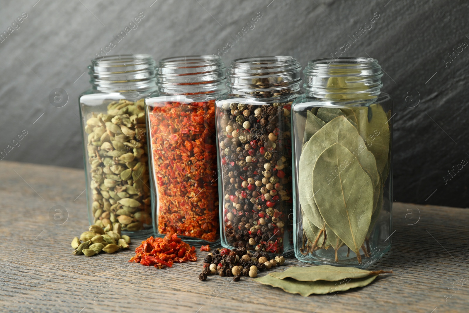 Photo of Different spices in glass jars on grey wooden table, closeup