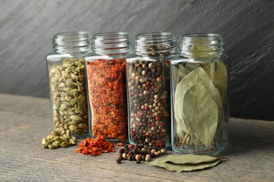 Different spices in glass jars on grey wooden table, closeup