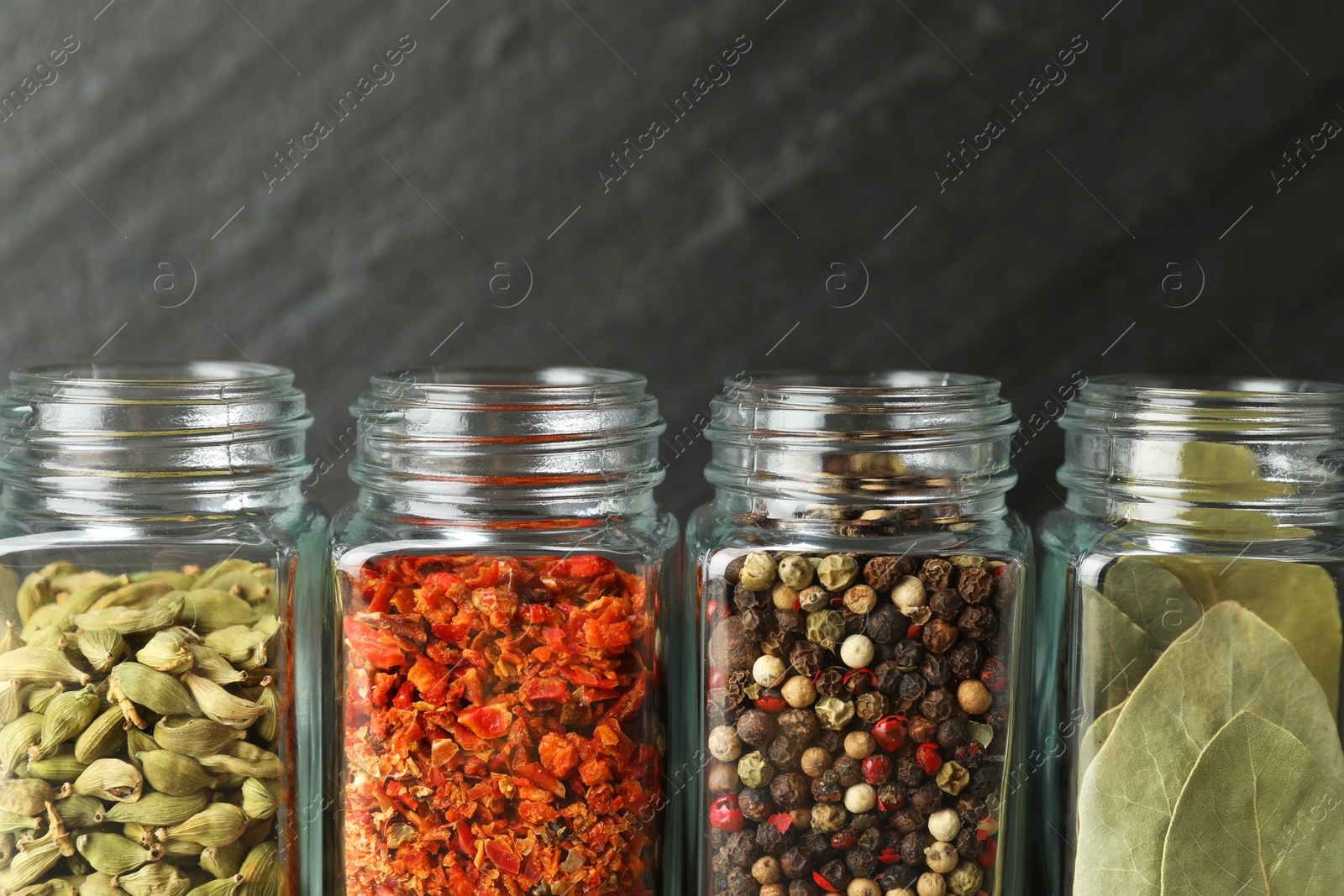 Photo of Different spices in glass jars on dark background, closeup