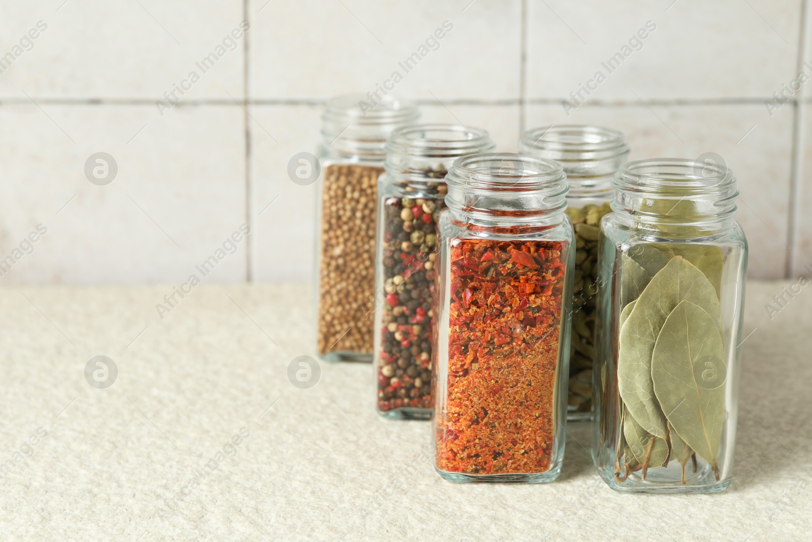 Photo of Different spices in glass jars on light textured table, closeup. Space for text