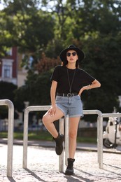 Photo of Young woman in stylish black hat and sunglasses on city street