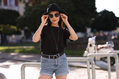 Photo of Young woman in stylish black hat and sunglasses on city street