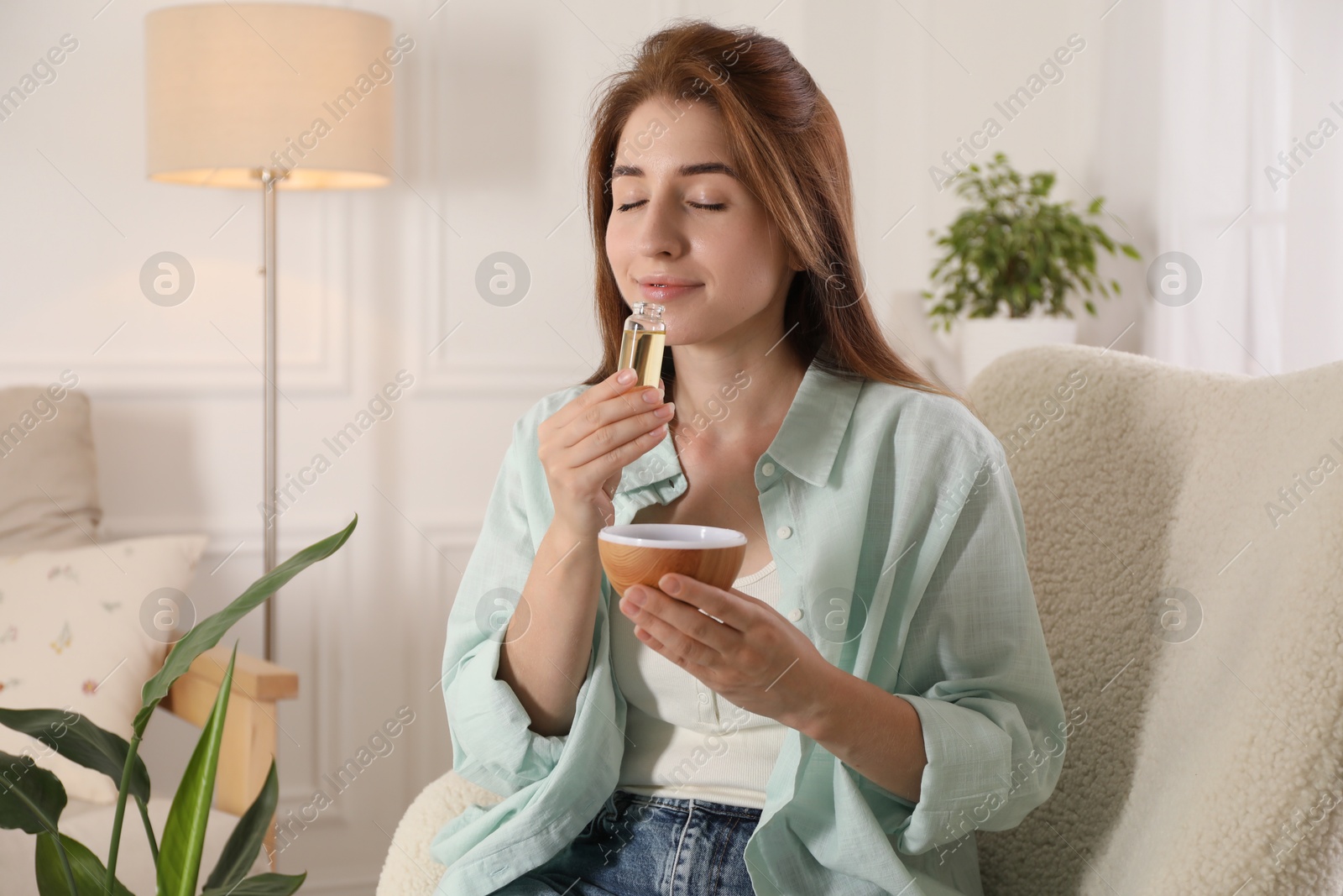 Photo of Woman with aroma diffuser and bottle of essential oil at home