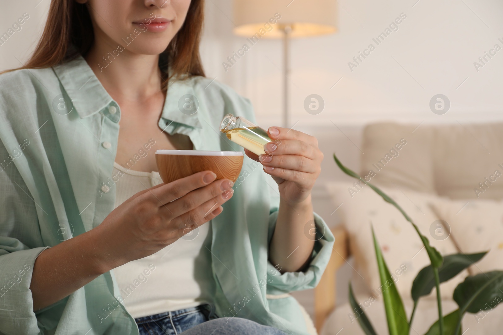 Photo of Woman adding essential oil to aroma diffuser at home, closeup