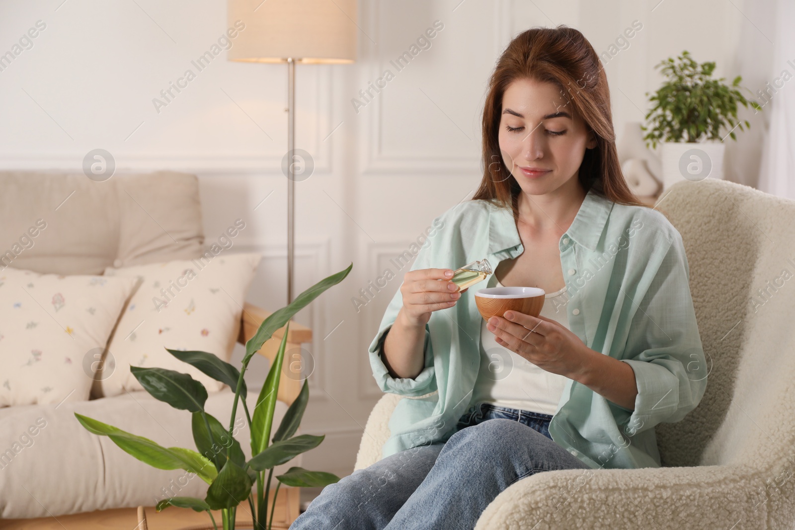 Photo of Woman adding essential oil to aroma diffuser at home