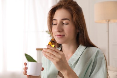 Photo of Woman with aroma diffuser and bottle of essential oil at home