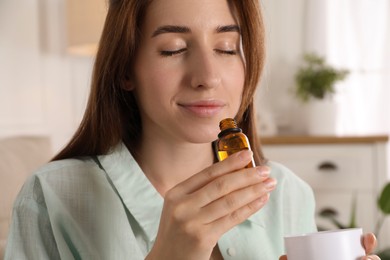 Woman with aroma diffuser and bottle of essential oil at home