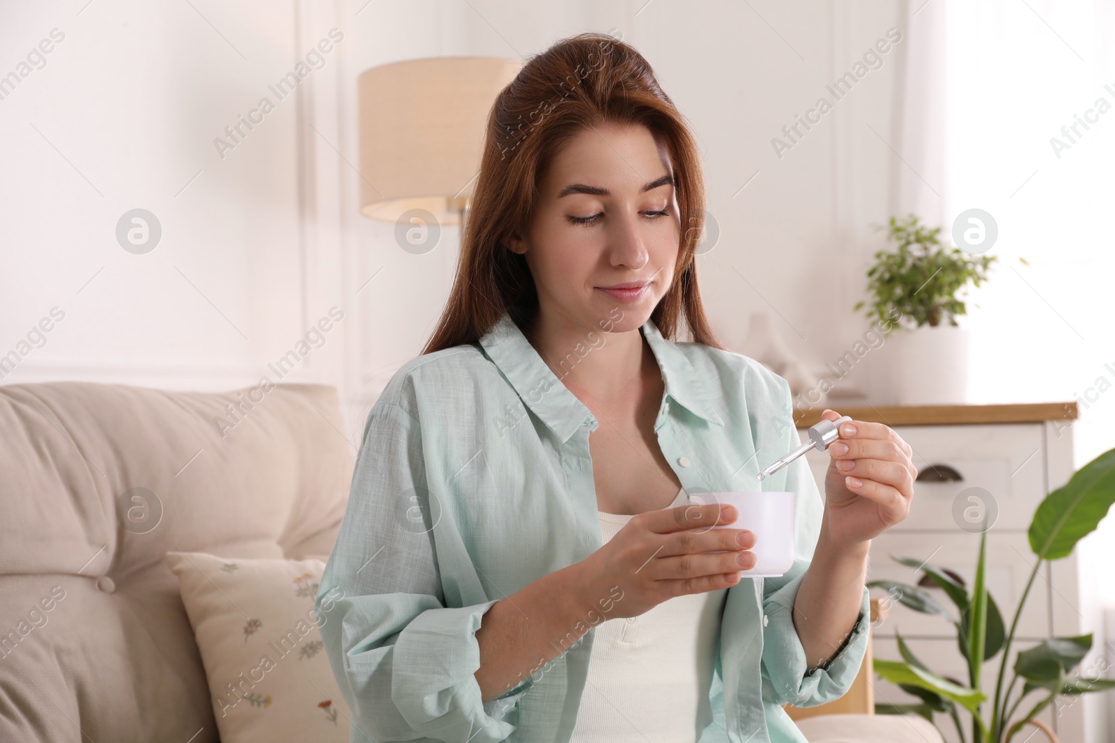 Photo of Woman adding essential oil to aroma diffuser at home