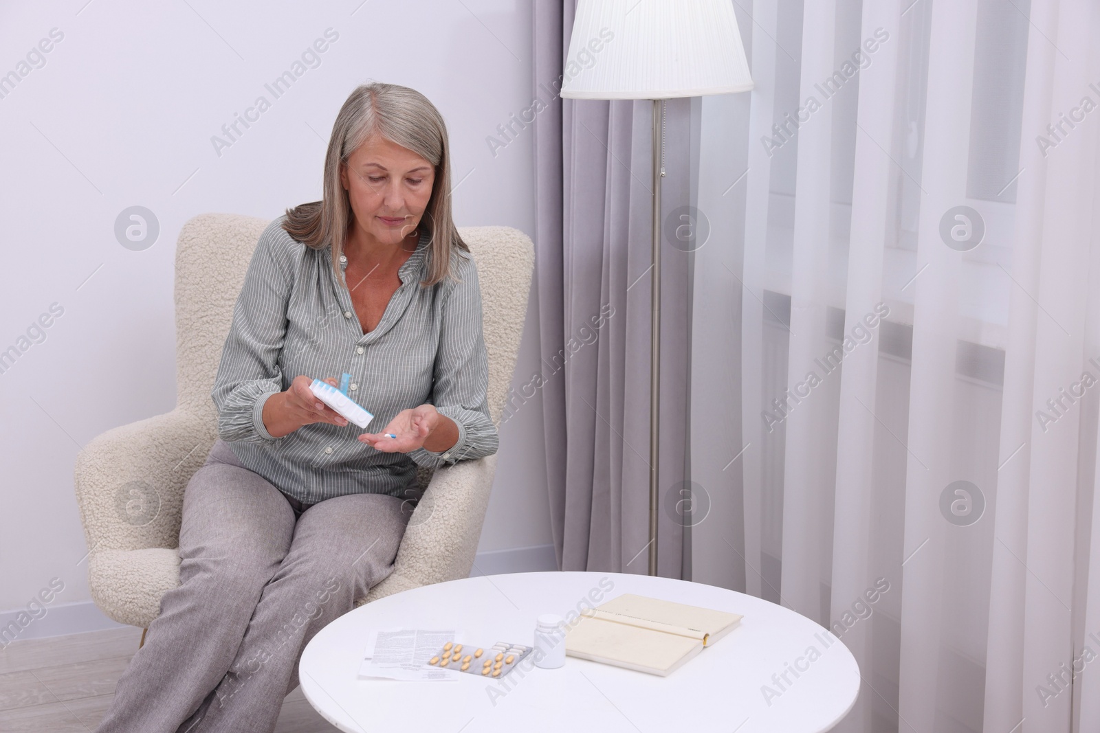 Photo of Senior woman with pills and organizer in armchair at home