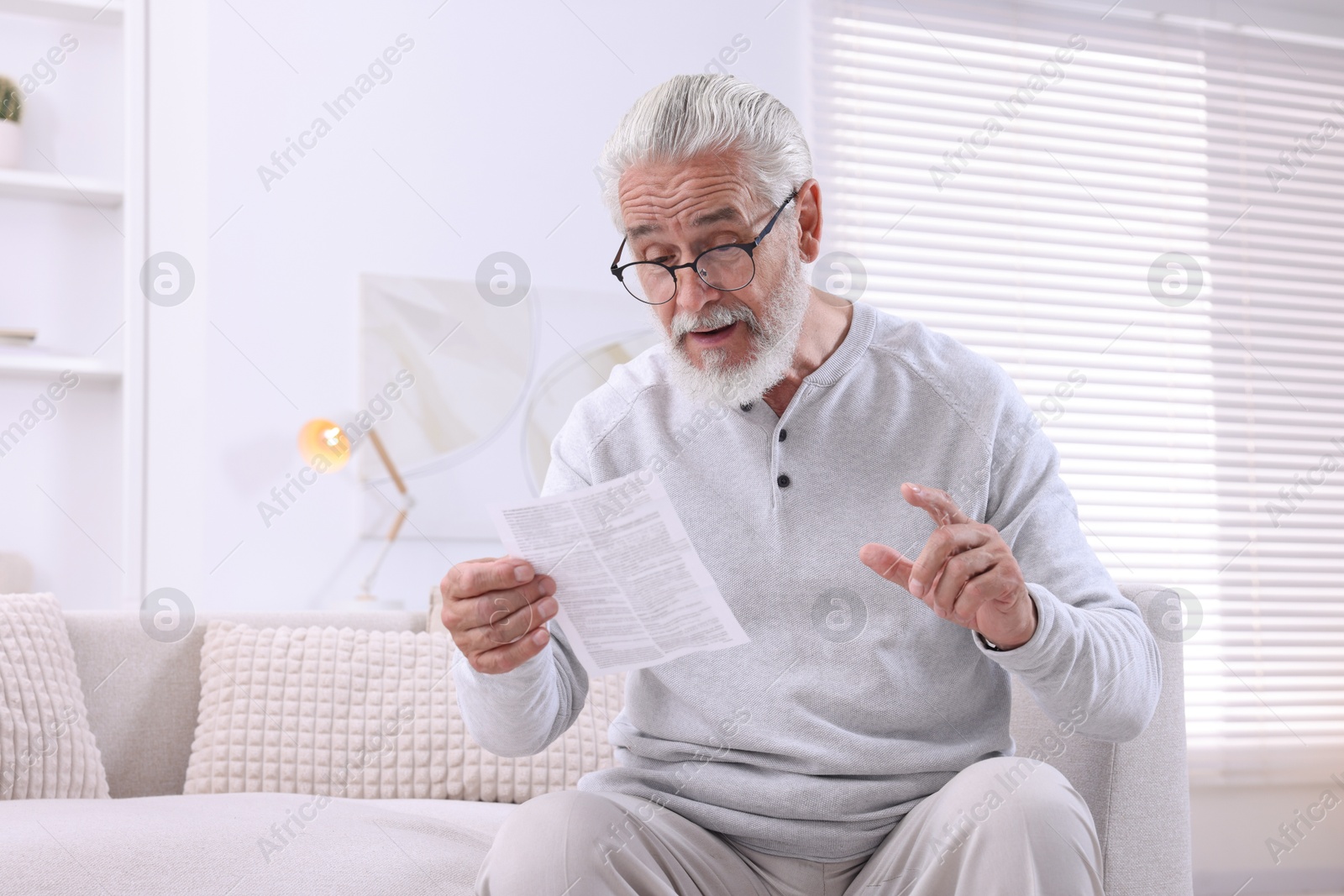 Photo of Senior man reading medicine instruction on sofa at home