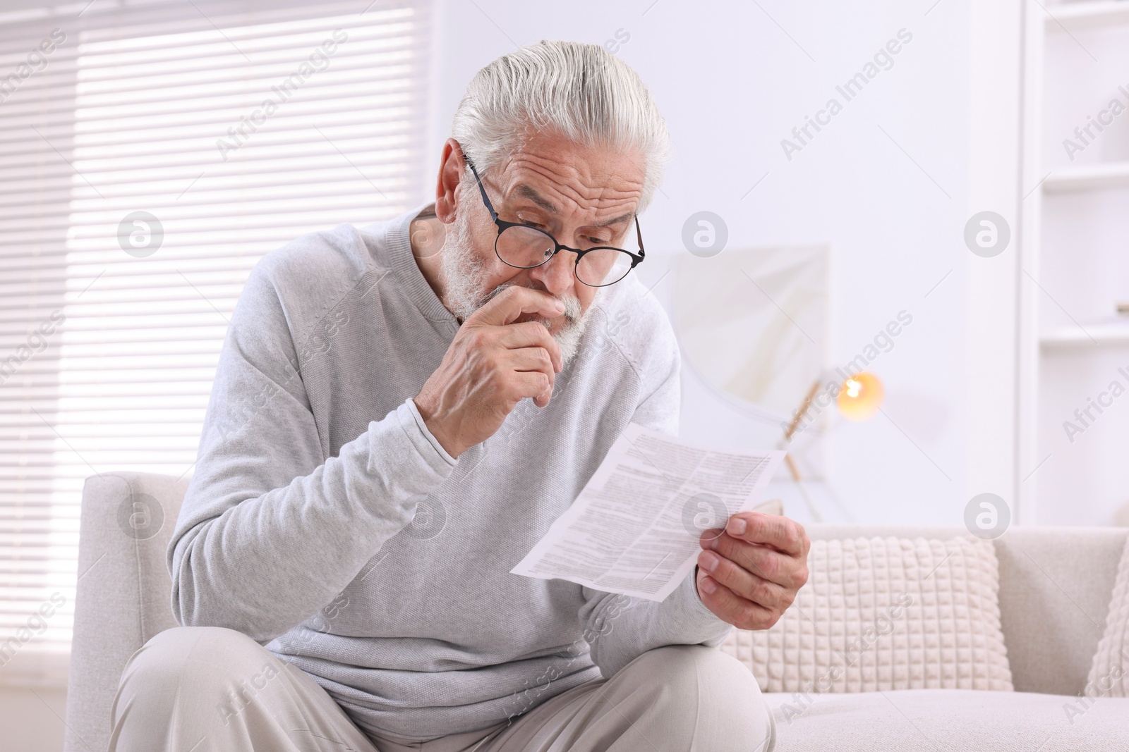 Photo of Senior man reading medicine instruction on sofa at home