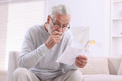 Photo of Senior man reading medicine instruction on sofa at home