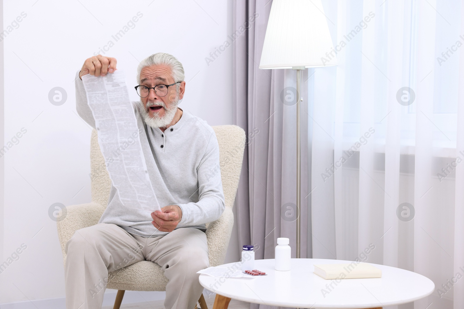 Photo of Senior man reading medicine instruction in armchair at home