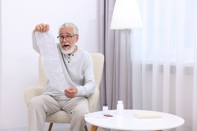 Senior man reading medicine instruction in armchair at home