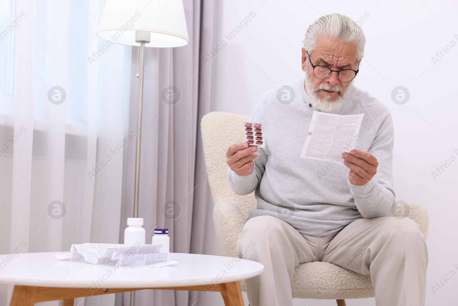 Photo of Senior man with pills reading medicine instruction in armchair at home