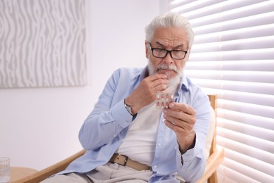 Senior man with glass of water taking pill at home