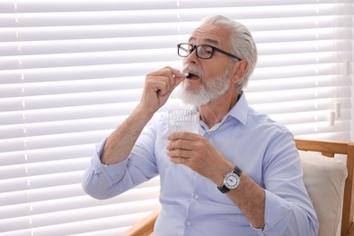 Photo of Senior man with glass of water taking pill at home