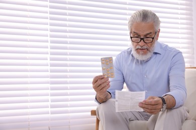 Senior man with pills reading medicine instruction at home, space for text